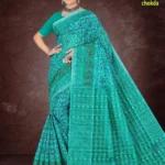 Woman draped in a turquoise Florence Varli Chokda saree by Sharda Lifestyle, featuring intricate tribal and geometric motifs, a matching blouse, and accessorized with oxidized silver jewelry, posed against a textured brown backdrop.