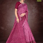 Woman wearing a deep pink Florence Varli Chokda saree by Sharda Lifestyle, featuring intricate traditional prints, a richly detailed pallu, and matching blouse, styled with silver jewelry against a brown textured backdrop.