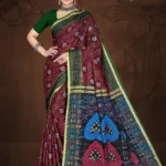 Model wearing maroon and green Singapore Gold saree with floral print and multicolor pallu featuring heart motifs and geometric designs